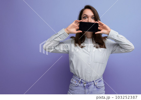 cute young brunette woman in shirt holding phone with screen forward on studio background cute young brunette woman in shirt holding phone with screen forward on studio background 103252387