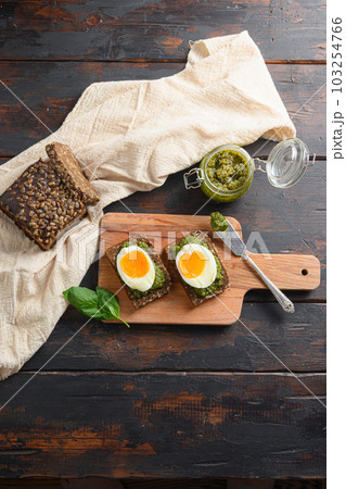 Fresh Green basil pesto in glass jar homemade on old rustic wood eggs panini bread with pesto knife  and hot sriracha sauce italian breakfast with ingredients green pesto top view vertical 103254766