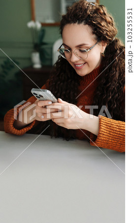 Young smiling woman wearing glasses holding a smartphone using cellphone modern technology, looking 103255531