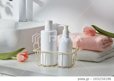 Personal hygiene concept with cosmetic container inside a basket displayed with few towels and pink flowers. Blank label for product mockup Personal hygiene concept with cosmetic container inside a basket displayed with few towels and pink flowers. Blank label for product mockup 103258196