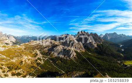 Rocky mountain peaks under blue sky with white clouds. Covered with grey sand deep canyons. Mountains near theThree Peaks of Lavaredo at sunset aerial view Rocky mountain peaks under blue sky with white clouds. Covered with grey sand deep canyons. Mountains near theThree Peaks of Lavaredo at sunset aerial view 103258839