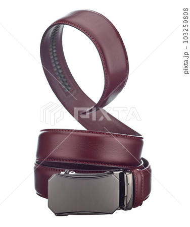 Beautiful leather belt made of burgundy leather, with a metal buckle-plate, beautifully twisted into a spiral, isolated on a white background. 103259808
