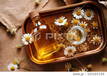 An overhead view of a wooden tray with chamomile flowers, essential oil, and dried petals, representing aromatherapy, natural skincare, and wellness concepts. Generative Ai 103265189