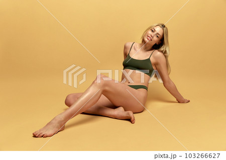 Wellness. Beautiful, young, blonde woman with fit, slim figure, body posing in green underwear against yellow studio background 103266627