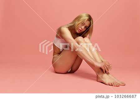 Portrait of young beautiful, blonde girl posing in white underwear against pink studio background. White, slim body 103266687