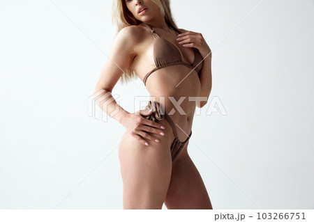 Cropped image of young, sensual woman with slim, fit body posing in swimsuit against grey studio background 103266751