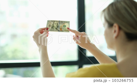 Woman studying watermarks on money dollars in front of window closeup 103266755