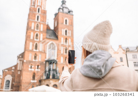 Young smile woman tourist In a stylish coat takes selfie on mobile phone on the market square in Krakow in Poland 103268341