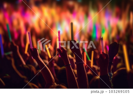 A close-up shot of hands holding glow sticks in the air at a rave party with a blurry crowd of people dancing in the background. Generative Ai A close-up shot of hands holding glow sticks in the air at a rave party with a blurry crowd of people dancing in the background. Generative Ai 103269105