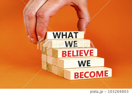 We become or believe symbol. Concept word What we believe We become on wooden block. Beautiful orange table orange background. Businessman hand. Business we become or believe concept. Copy space. 103269803