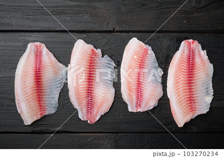 Raw tilapia fish fillet meat, on black wooden background, top view Raw tilapia fish fillet meat, on black wooden background, top view 103270234