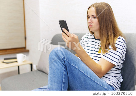 Happy young woman is using mobile phone while sitting a couch at home. Happy young woman is using mobile phone while sitting a couch at home. 103270516