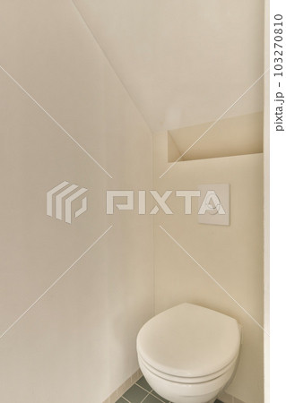 a toilet in the corner of a room with white walls and green tiles on the floor, there is an electrical outlet 103270810