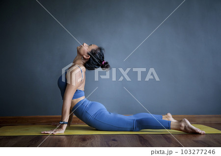 asian woman doing yoga pose in home living home against empty gray wall 103277246