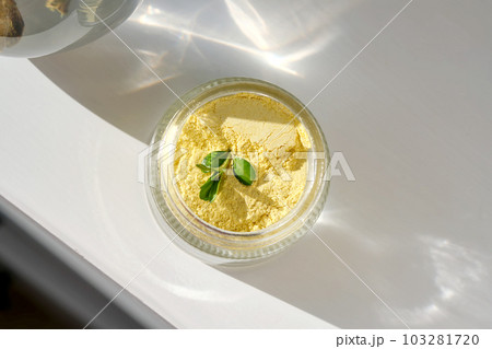 An open jar of a yellow turmeric facial scrub showing off its texture. An open jar of a yellow turmeric facial scrub showing off its texture. 103281720