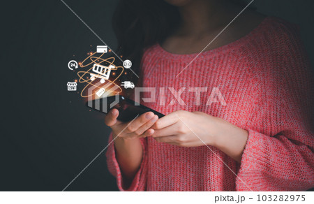 Woman in pink dress using smartphone show screen virtual info graphics with business ecommerce and trolley cart icons, Internet network online shop store. Technology online shopping business concept. 103282975