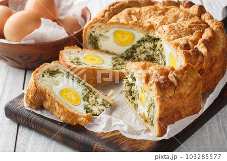 Portioned traditional Italian Easter cake or tart with spinach, ricotta and whole eggs closeup on the wooden board. Horizontal 103285577