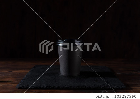 Black cardboard cup with lid. Black glass on a black background. Coffee glass on a slate tray. 103287590