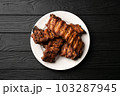 Freshly cooked pork ribs on a white round plate on a black wooden table in the background. Close up 103287945