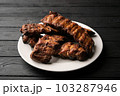 Freshly cooked pork ribs on a white round plate on a black wooden table in the background. Close-up 103287946