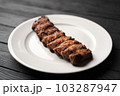 Freshly cooked pork ribs on a white round plate on a black wooden table in the background. Close-up 103287947