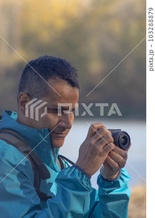 Portrait of traveler man at lake in autumn taking a photo with the digital camera 103288879