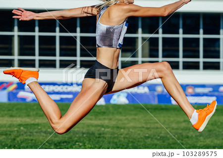 close-up female athlete jumping triplejump in summer athletics championships on background green field close-up female athlete jumping triplejump in summer athletics championships on background green field 103289575