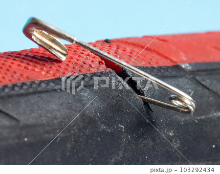 The bicycle tire is damaged by a safety pin, close up view. 103292434