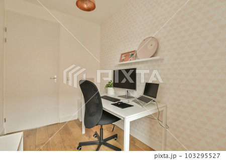 a room with a desk, chair and computer on the floor in front of a white wallpapered wall 103295527