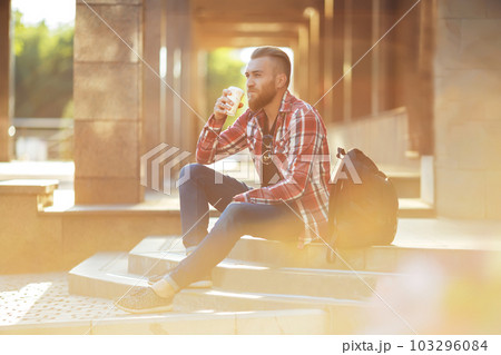 Handsome young man holding mobile phone and drinking coffee while sitting in the rest area. 103296084