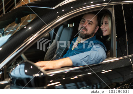Happy married couple testing new car in car showroom.  103296635
