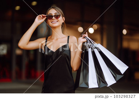 Fashion woman enjoying shopping. Elegant woman wears black dress holding black and white shopping bags. 103298327