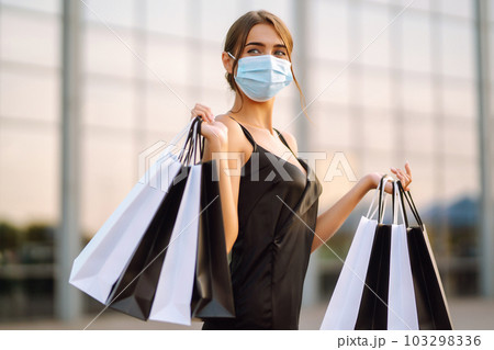 Beautiful woman in protective sterile medical mask with shopping bags near shopping center.Covid- 2019. Beautiful woman in protective sterile medical mask with shopping bags near shopping center.Covid- 2019. 103298336