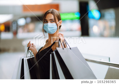 Fashionable woman in protective medical mask with shopping bags walking in the mall. Covid-19. 103298365