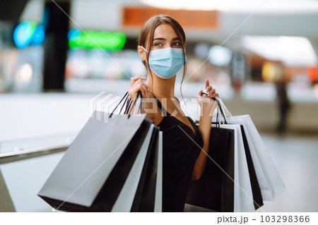 Beautiful fashionable woman in protective medical mask with shopping bags walking near mall. Covid-19. Beautiful fashionable woman in protective medical mask with shopping bags walking near mall. Covid-19. 103298366