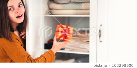 Funny girl makes surprise, hides a gift in the closet. Funny girl makes surprise, hides a gift in the closet. 103298900