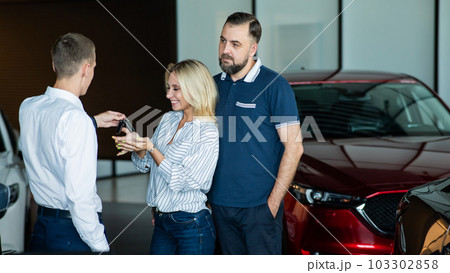 The seller hands over the car keys to the buyers. The couple bought a new car. The seller hands over the car keys to the buyers. The couple bought a new car. 103302858