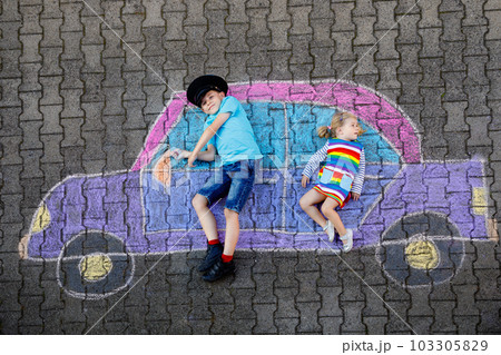 Two little children, kid boy and toddler girl having fun with with car picture drawing with colorful chalks on asphalt. Siblings painting on ground and playing together. Creative leisure for children 103305829