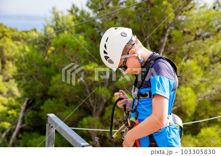 School boy preparing for zipline adventure. Happy active child put safety helmet on head. Summer fun with climbing in mountains. 103305830