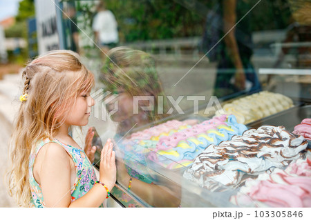 Happy preschool girl choosing and buying ice cream in outdoor stand cafe. Cute child looking at different sorts of icecream. Sweet summer dessert on family vacations. Summertime. 103305846