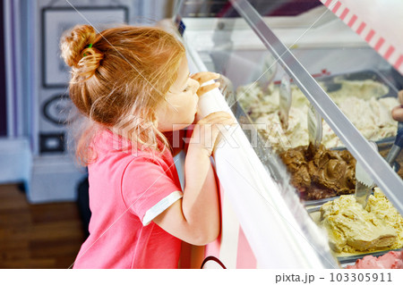 Cute little toddler girl choosing and buying ice cream in a cafe. Happy baby child looking at different sorts of icecream. Sweet home made dessert Cute little toddler girl choosing and buying ice cream in a cafe. Happy baby child looking at different sorts of icecream. Sweet home made dessert 103305911