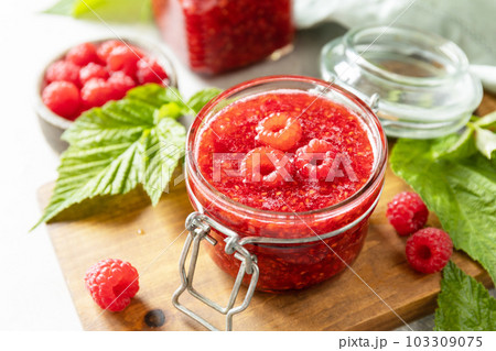 Homemade preservation. Delicious raspberries jam or jelly and fresh raspberries on a stone table. Homemade preservation. Delicious raspberries jam or jelly and fresh raspberries on a stone table. 103309075