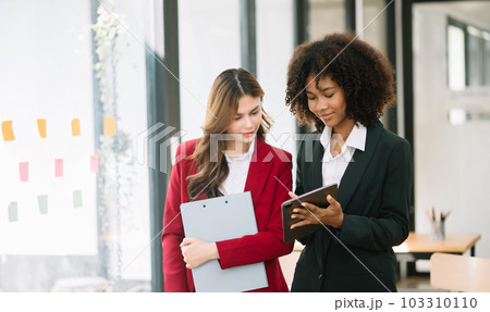 Businesswomen work and discuss their business plans. A Human employee explains and shows her colleague the results paper in modern office.. 103310110