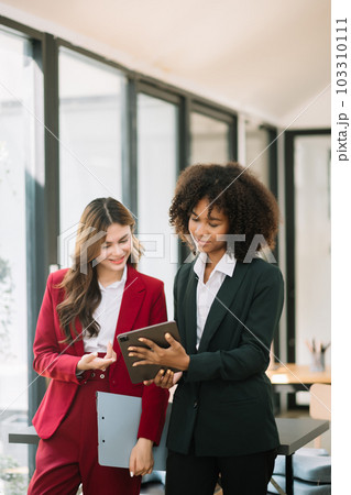 Businesswomen work and discuss their business plans. A Human employee explains and shows her colleague the results paper in modern office.. 103310111