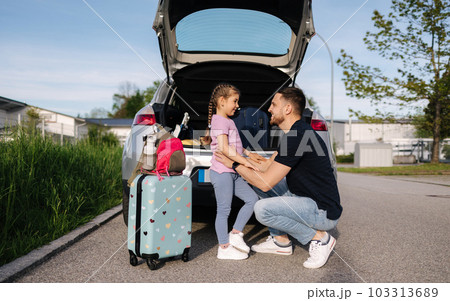 Dad and his daughter stand by the open trunk of their car and preparing for journey while mom turns on the alarm at home 103313689