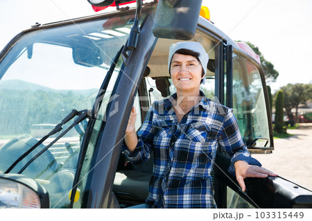 Confident female farm owner driving tractor 103315449