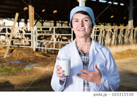 Female quality expert is standing in uniform and checking the quality of milk at the farm. Female quality expert is standing in uniform and checking the quality of milk at the farm. 103315530