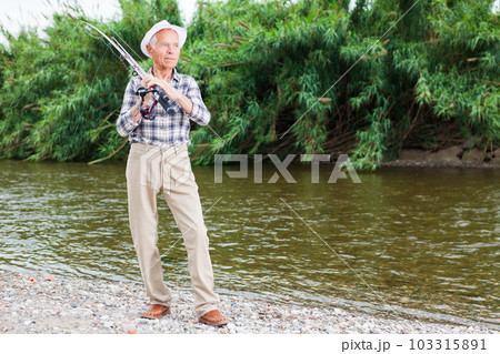 Mature fisherman with rod at riverside 103315891