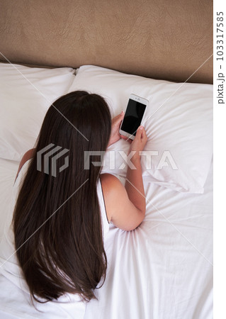 A young girl in white underwear lying on a bed and uses a smartphone. A young girl in white underwear lying on a bed and uses a smartphone. 103317585