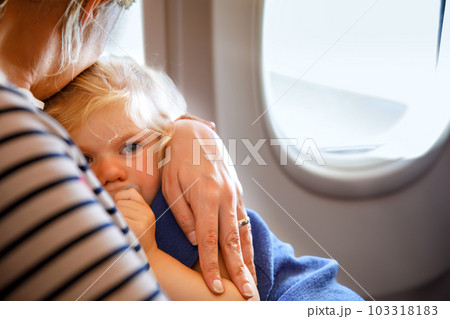 Woman traveling with little child by airplane. Sad tired toddler girl sitting with mum by aircraft window. Motherhood concept. Crying baby. Woman traveling with little child by airplane. Sad tired toddler girl sitting with mum by aircraft window. Motherhood concept. Crying baby. 103318183